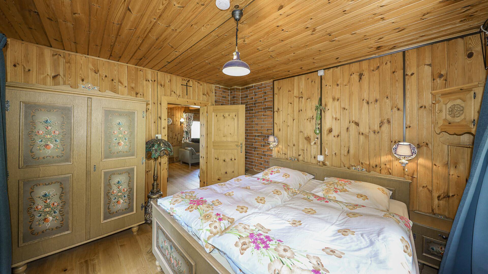 Gemütliches Schlafzimmer mit Doppelbett, Holztäfelung und traditionellem, bemaltem Kleiderschrank.