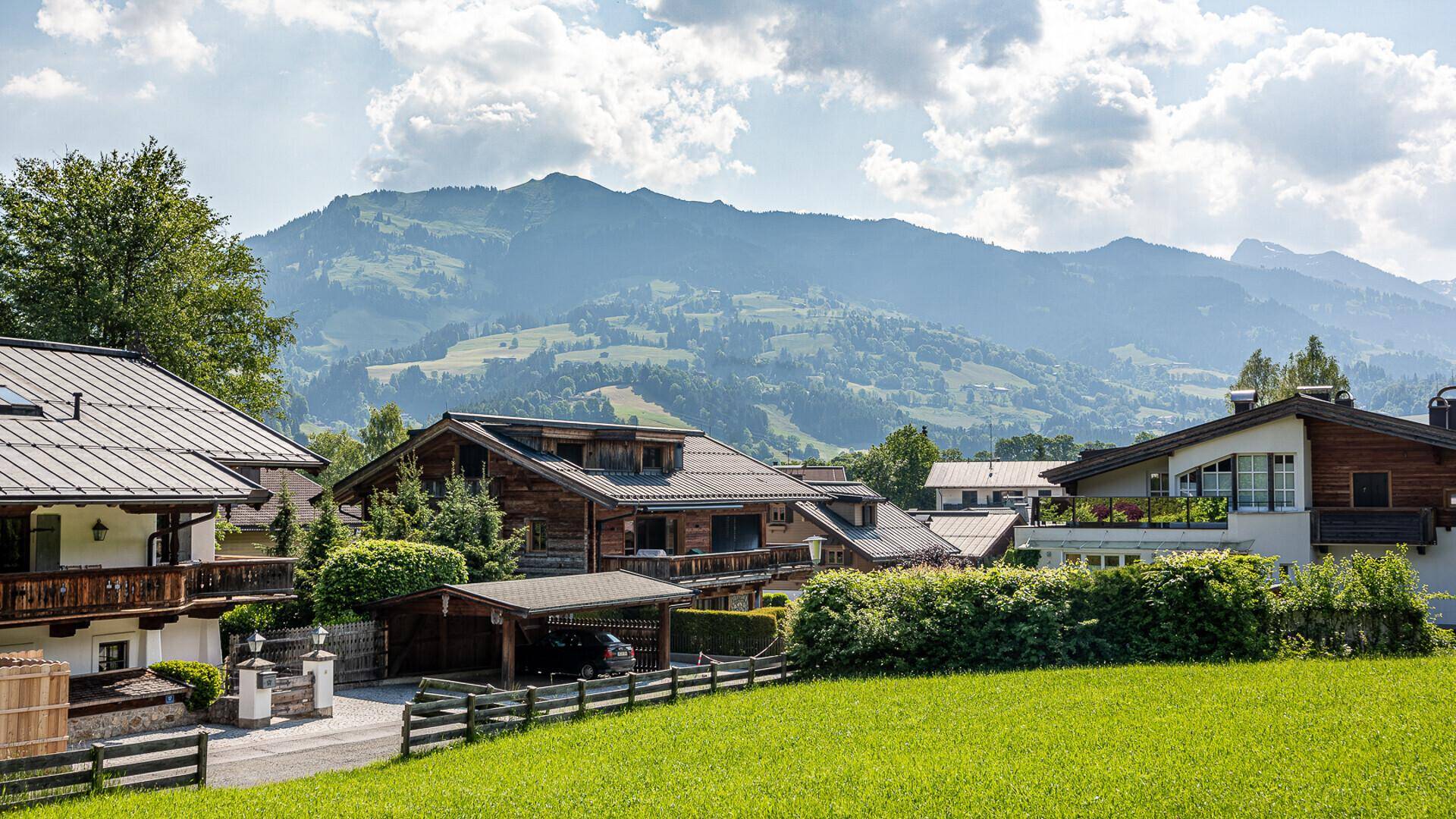 Idyllische Ansicht von Häusern in einer Berglandschaft mit grünen Wiesen und klarem Himmel.