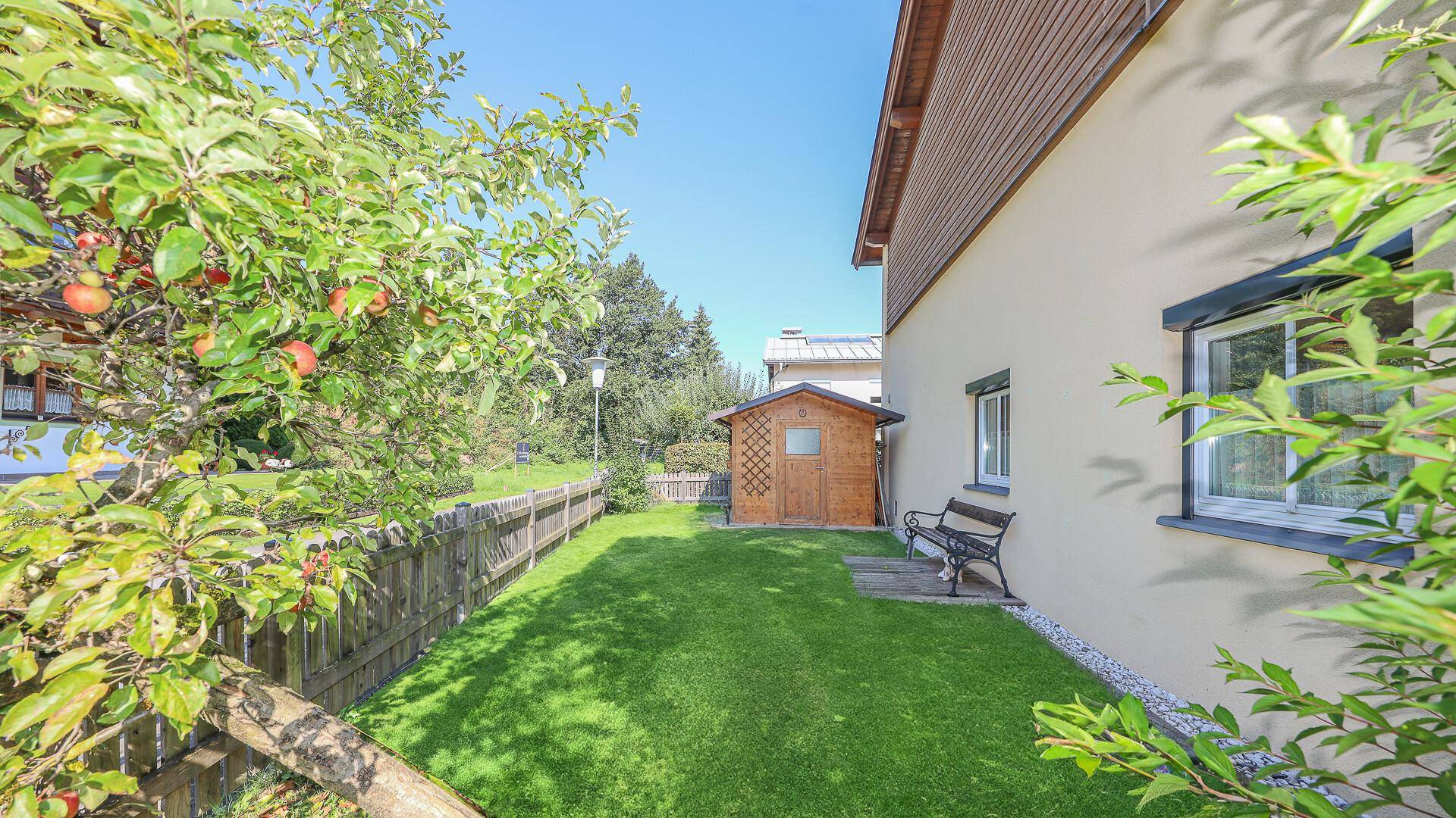 Seitlicher Gartenbereich mit Rasenfläche, Obstbäumen und einem kleinen Gartenhaus.