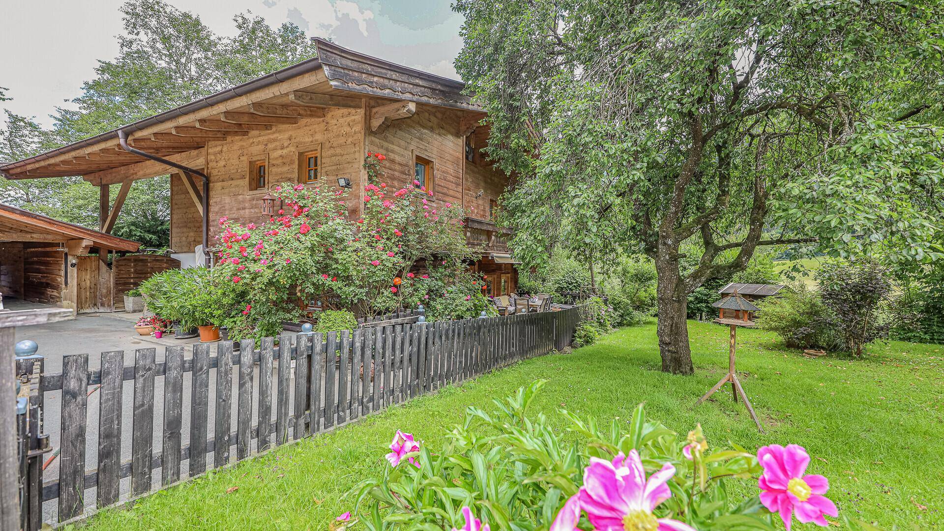 Traditionelles Holzhaus mit blühendem Garten, Rasenfläche und gemütlichem Sitzbereich im Freien.