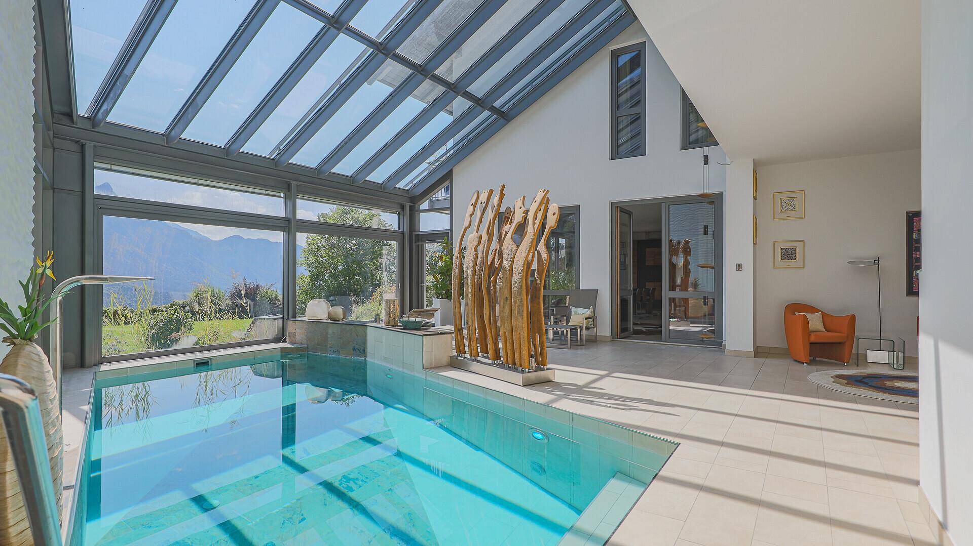 Geräumiger Innenpoolbereich mit Glasdach, großen Fenstern und Blick auf die umliegende Natur.