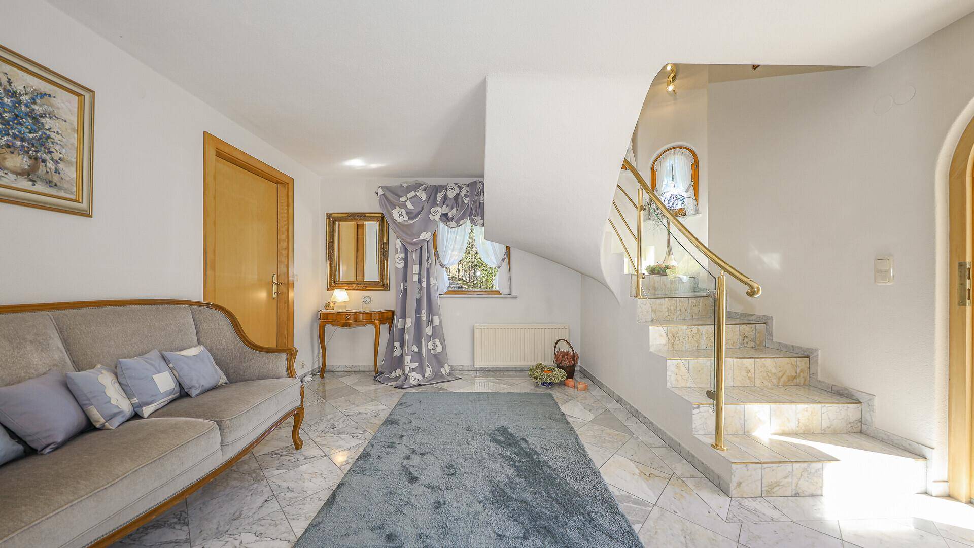 Geräumiger Eingangsbereich mit Marmorboden, geschwungener Treppe und Sitzgelegenheit.