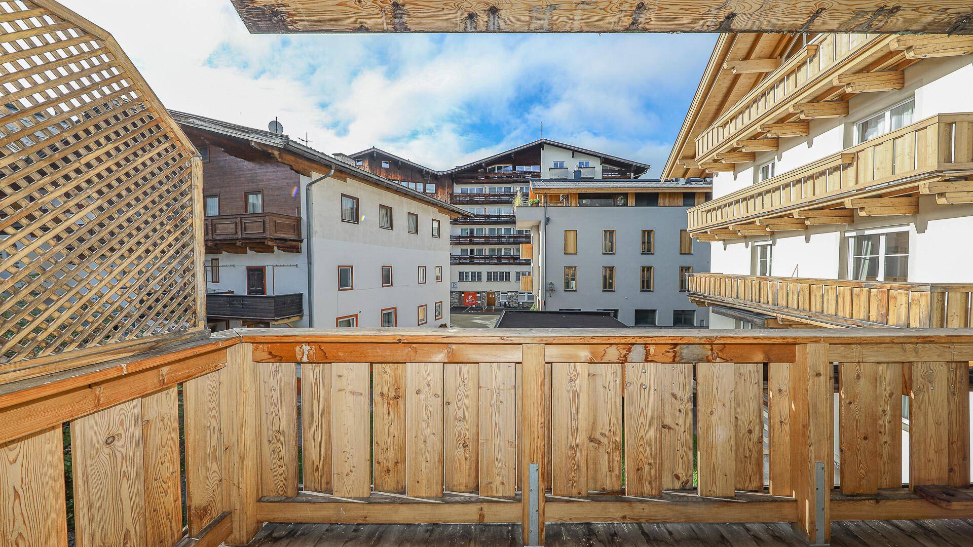 Balkon mit Holzgeländer und Blick auf die umliegenden Gebäude und den Himmel.