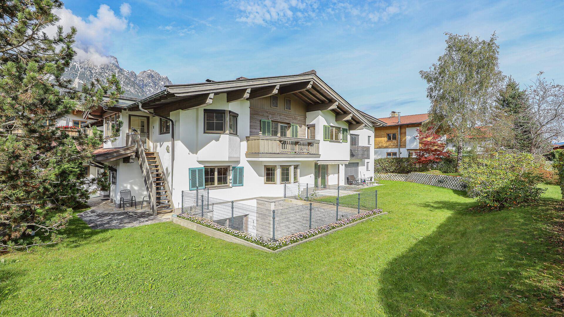 Rückansicht des Hauses mit weißer Fassade, Garten und Blick auf die umliegende Berglandschaft.