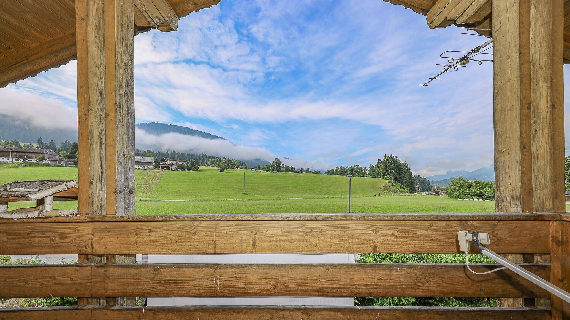 Überdachter Holzbalkon mit weitem Blick auf die grüne Landschaft und die Berge.