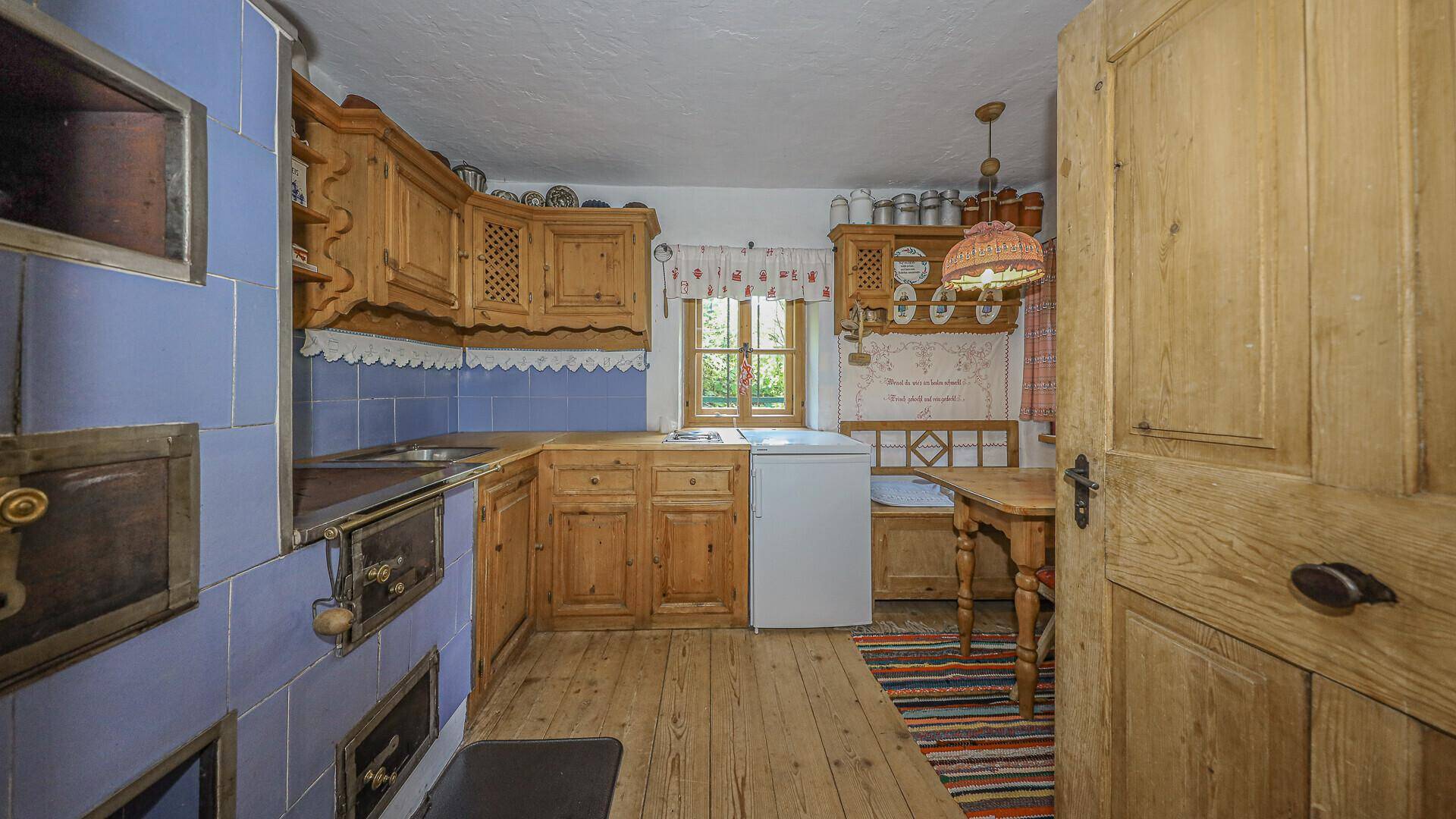 Rustikale Küche im Originalzustand mit Holzschränken, blau gefliestem Bereich und traditionellem Herd.