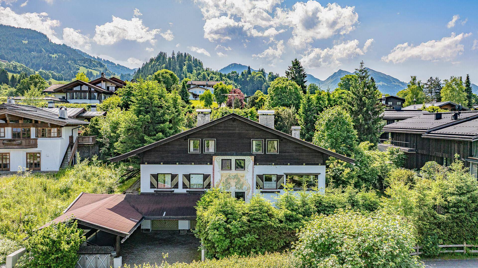 Traditionelles Chalet mit Holzbalkonen und Satteldach, umgeben von grünen Bäumen und Bergen.