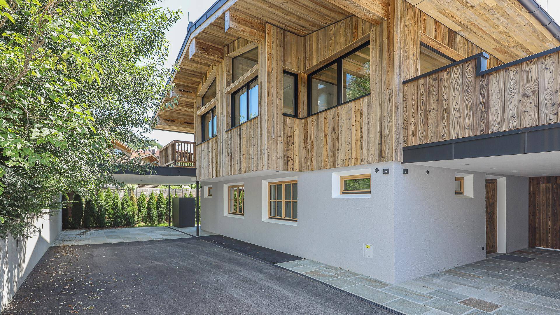 Moderne Holzfassade mit großen Fenstern und überdachtem Parkplatzbereich.