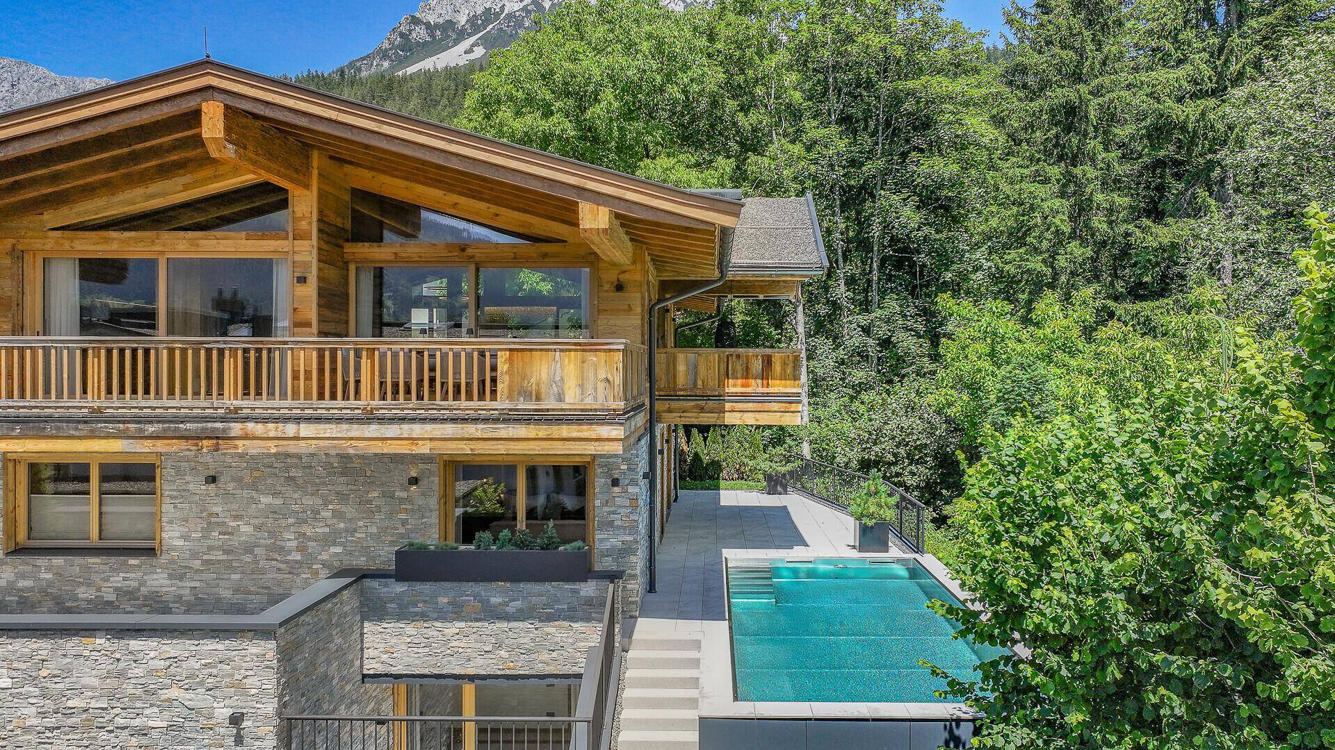 Seitenansicht des Chalets mit Natursteinfassade, Holzverkleidung und einem eleganten Außenpool.