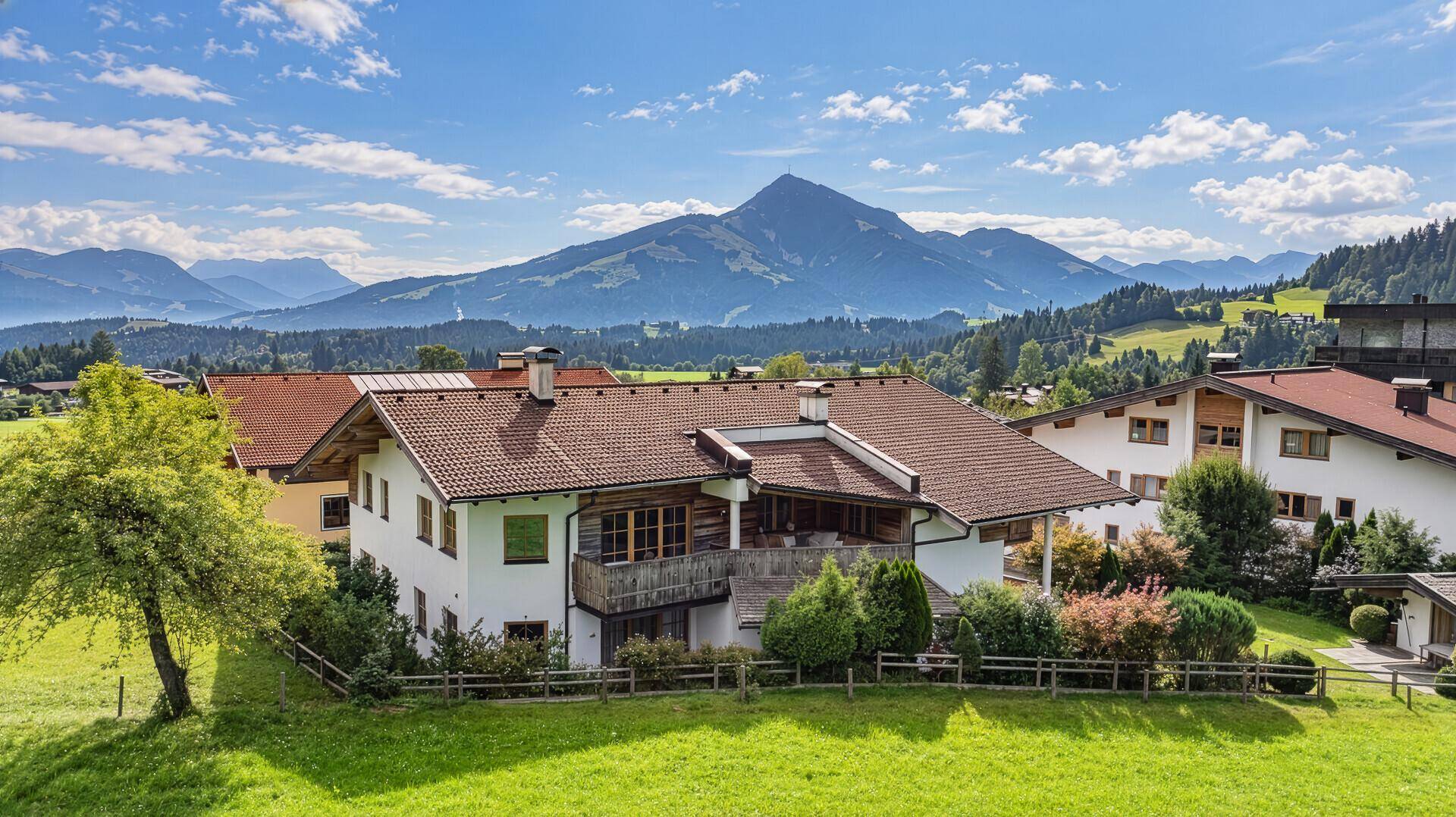 Traditionelles Wohnhaus umgeben von grünen Wiesen und mit weitem Blick auf die Bergwelt.