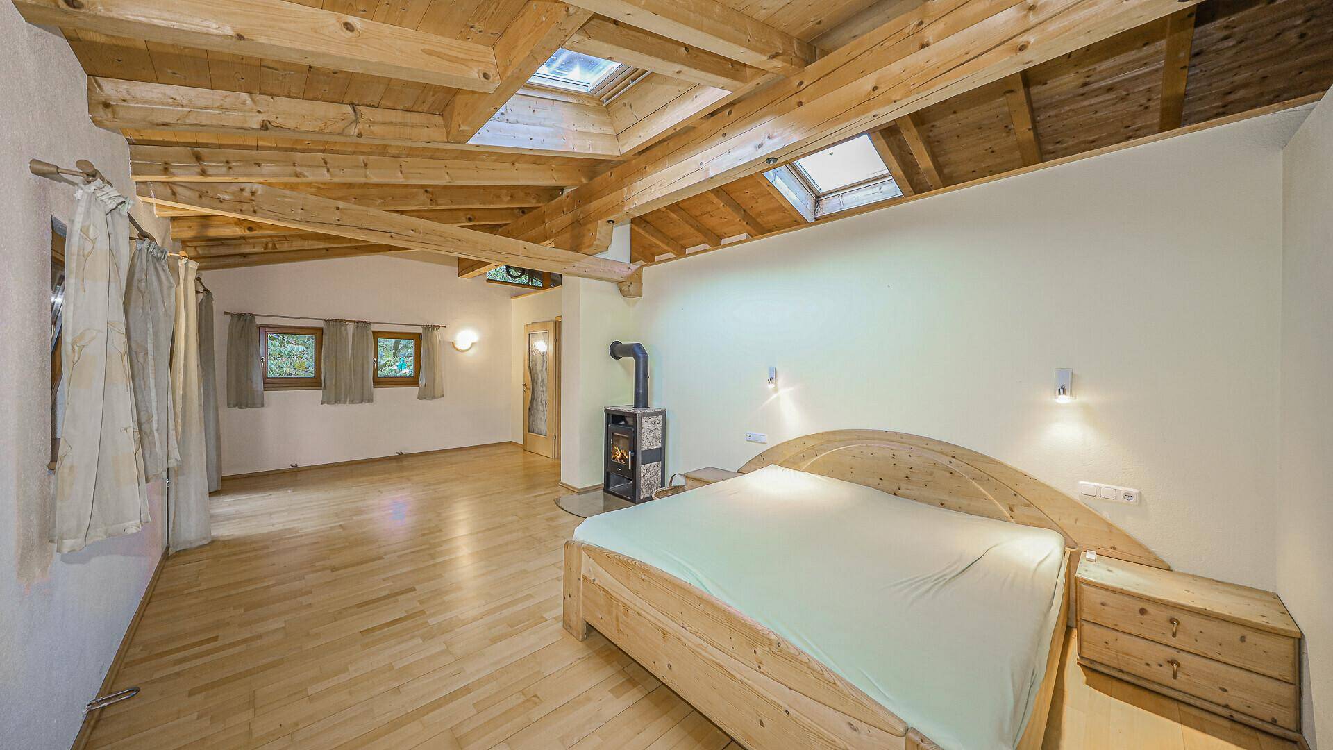 Gemütliches Schlafzimmer mit Holzbalkendecke, Dachfenstern und Kaminofen, ideal für erholsame Nächte.
