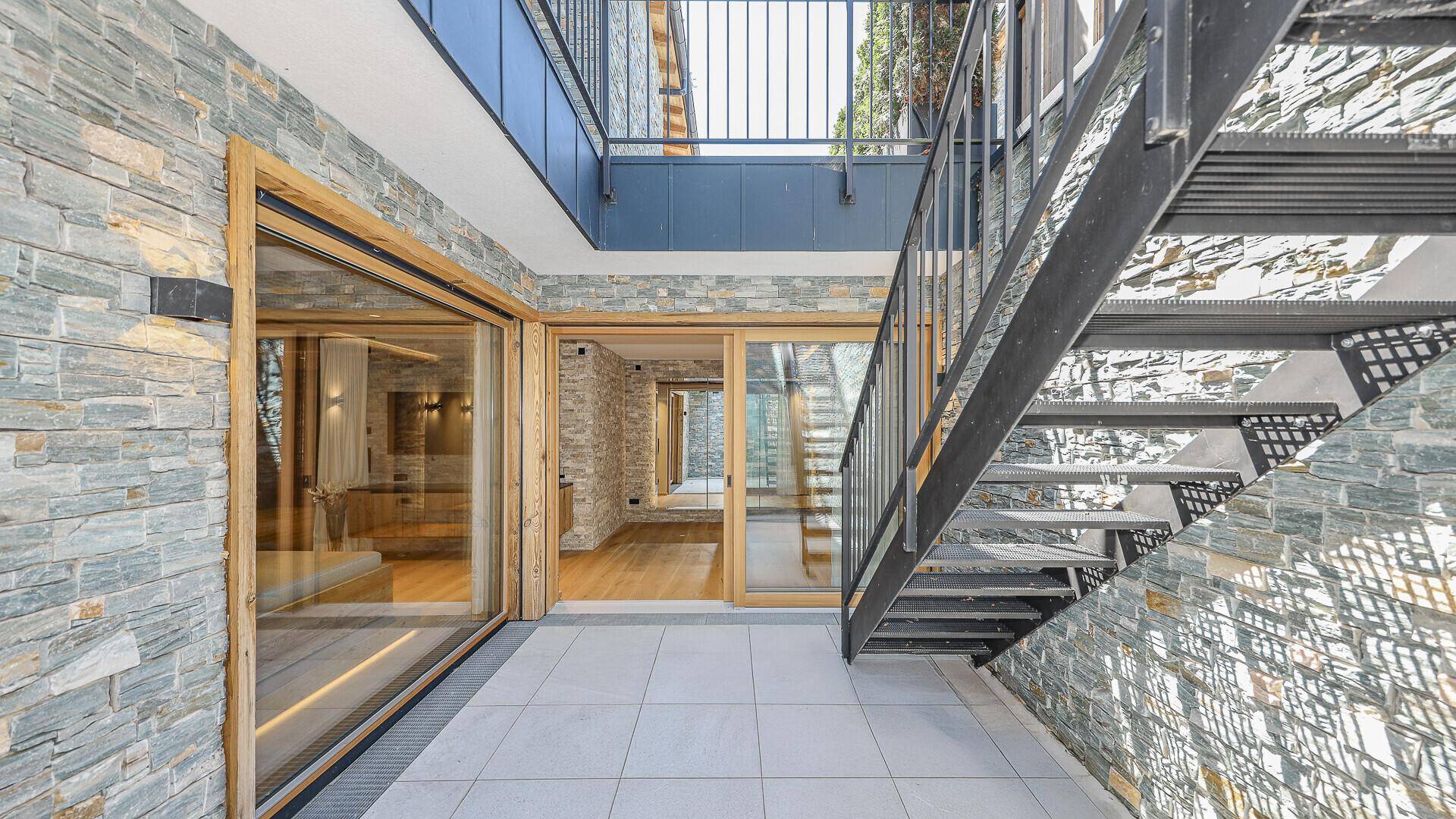 Außenbereich mit Steinfassade, Holzfenstern und einer modernen Metalltreppe.