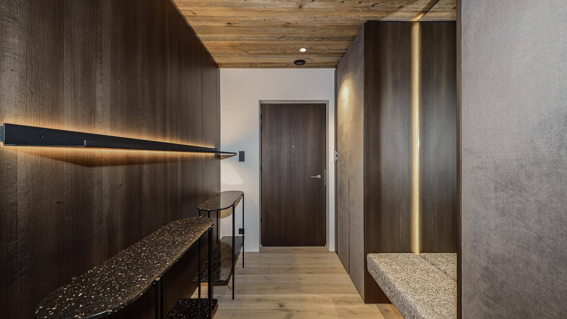 Moderner Eingangsbereich mit dunklen Holzpaneelen, heller Holzdecke und integrierter Sitzbank.