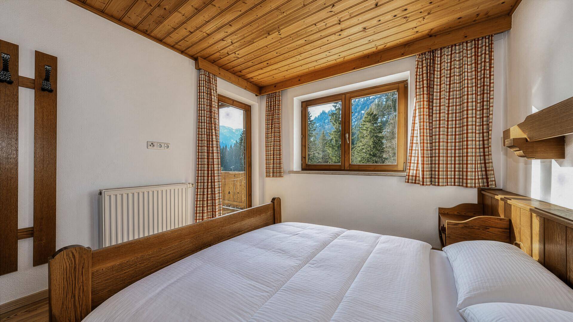 Gemütliches Schlafzimmer mit Holzbett, Holzbalkendecke und Bergblick.