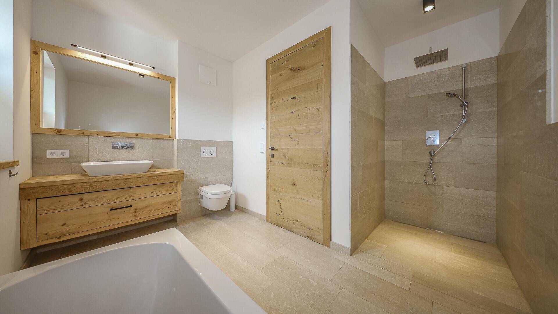 Helles Badezimmer mit Holzwaschtisch, Badewanne und großer ebenerdiger Dusche.