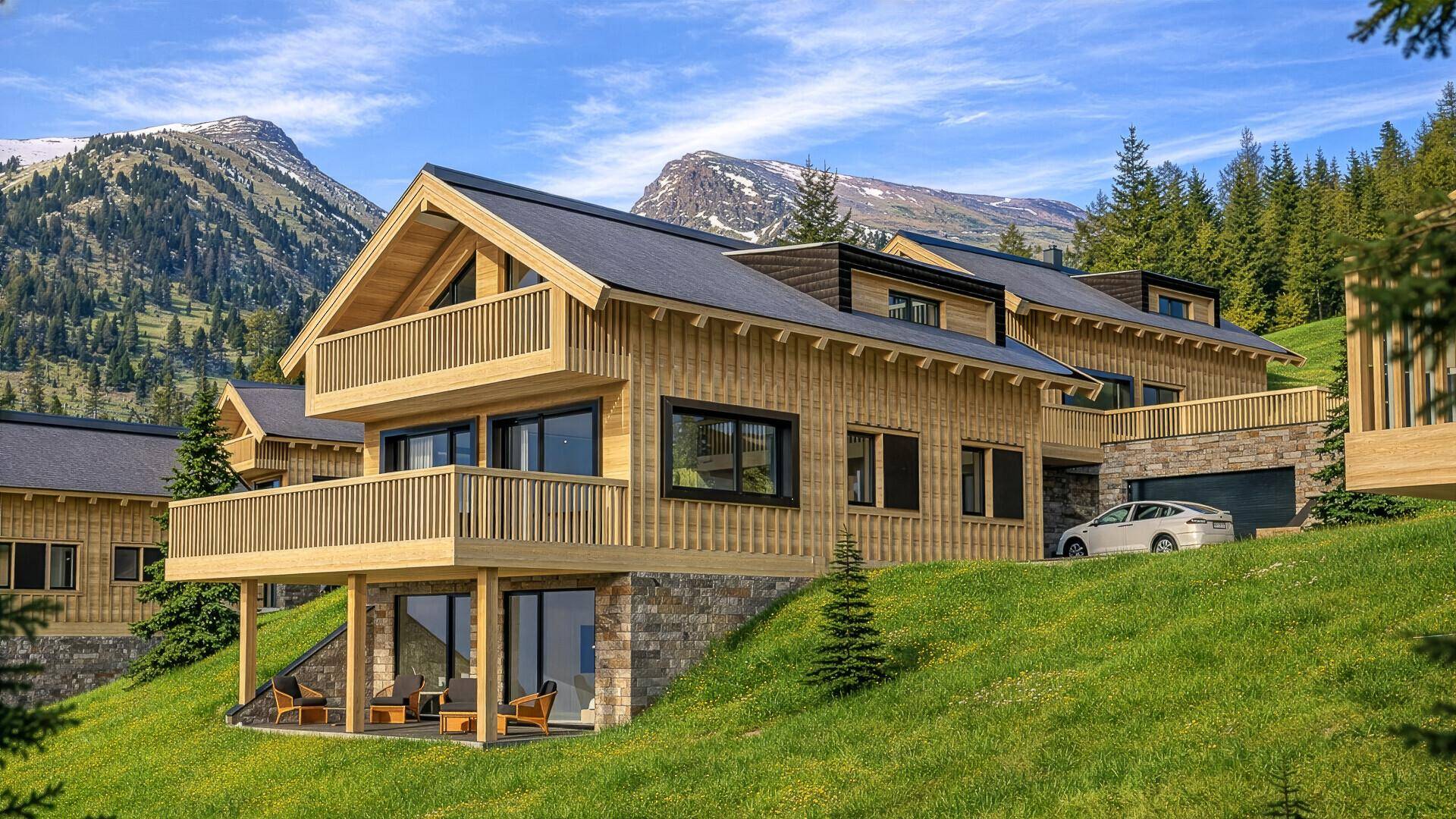 Modernes Holzchalet mit Balkonen und einer Terrasse, eingebettet in eine grüne Berglandschaft.