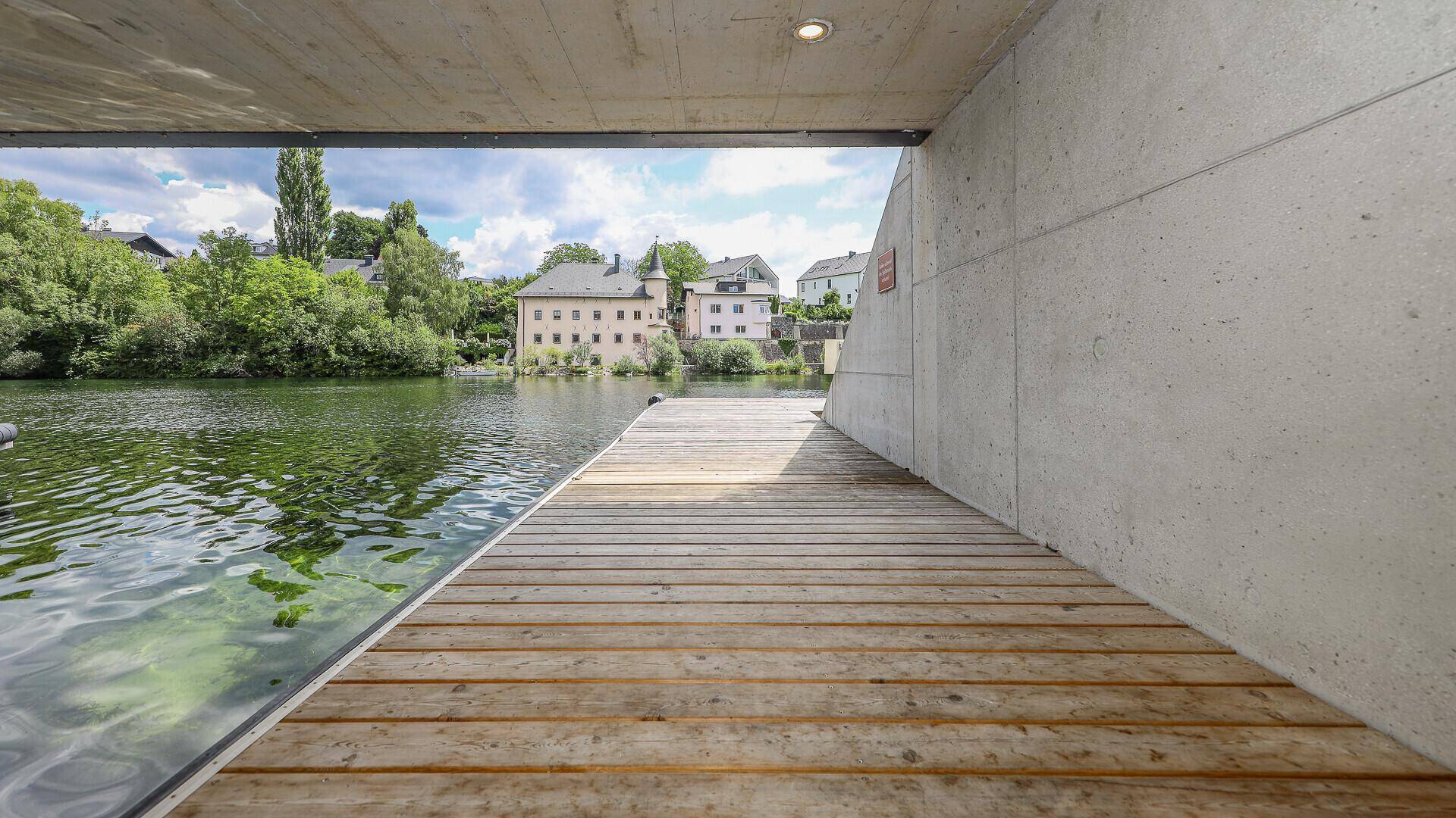Holzsteg am Wasser mit Blick auf historische Gebäude und grüne Ufer.