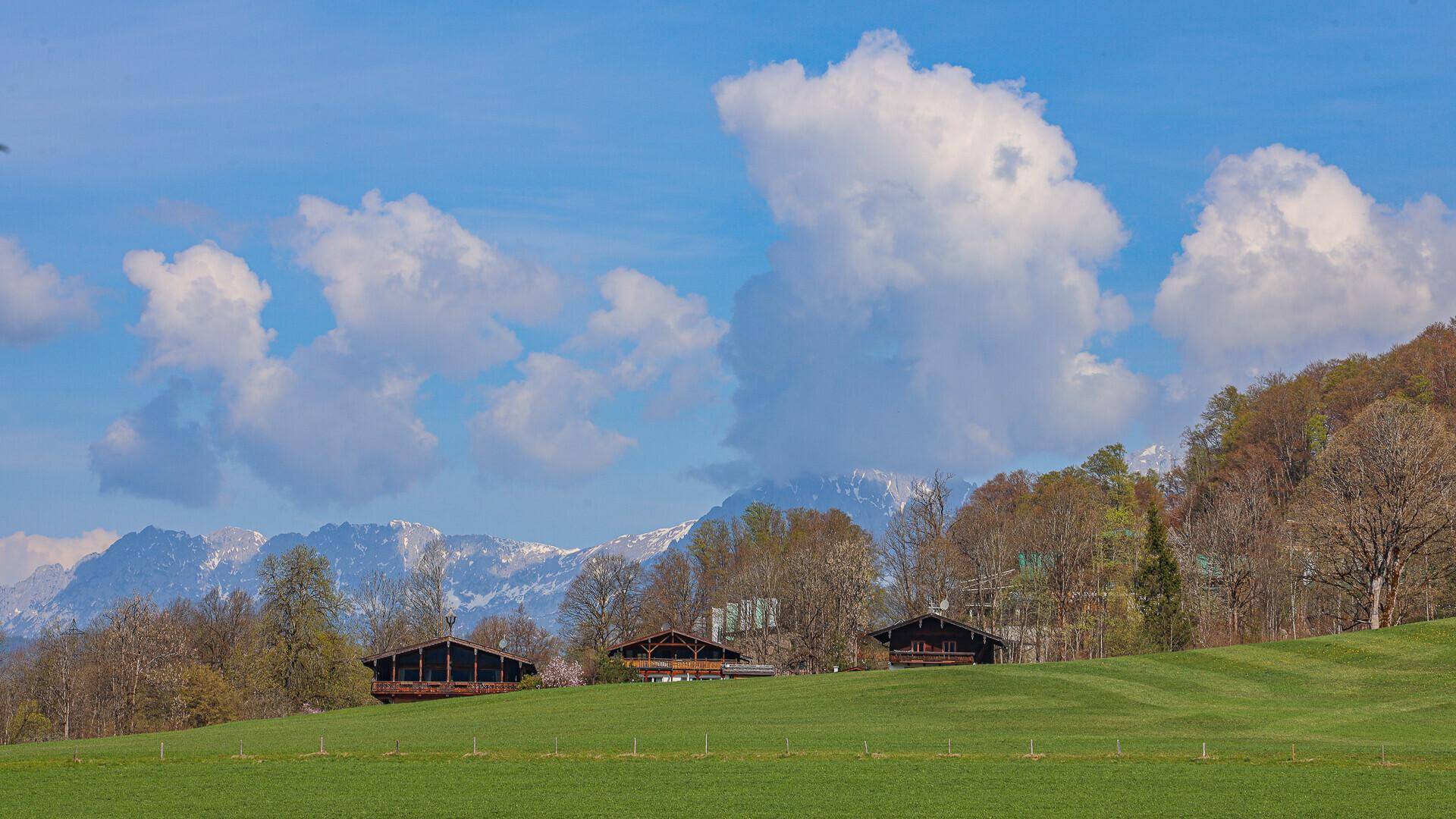 Idyllische Landschaft mit grünen Feldern, traditionellen Häusern und majestätischen Bergen unter Wolken.