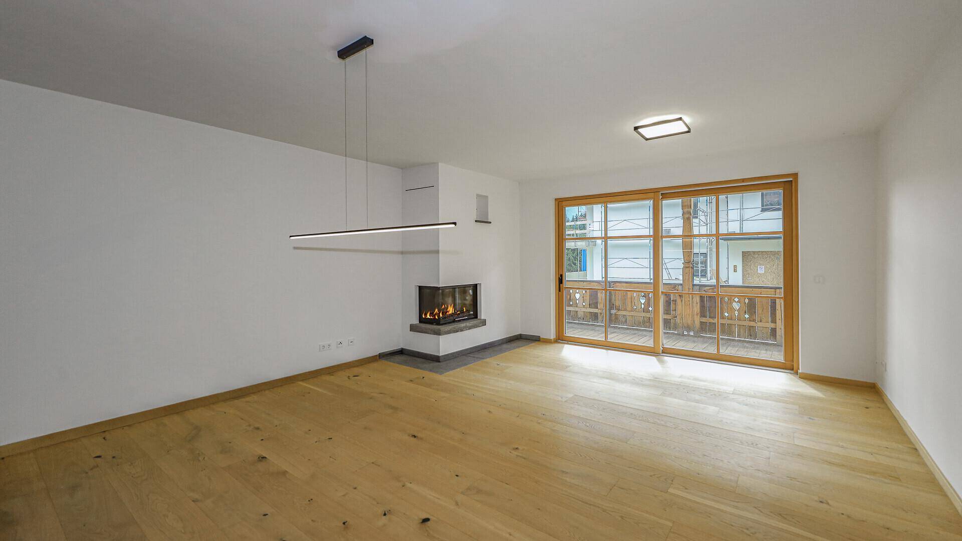 Heller Wohnbereich mit Holzboden, Kamin und Zugang zu einem Balkon.