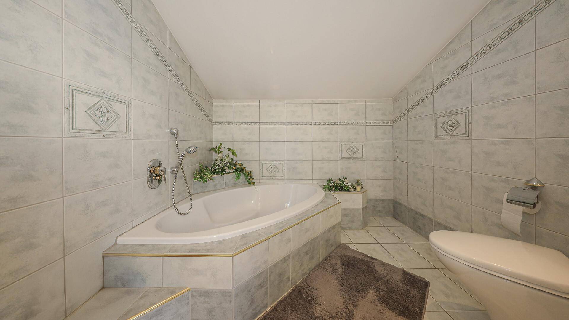 Geräumiges Badezimmer mit eingebauter Badewanne, hellen Fliesen und Dachschräge.