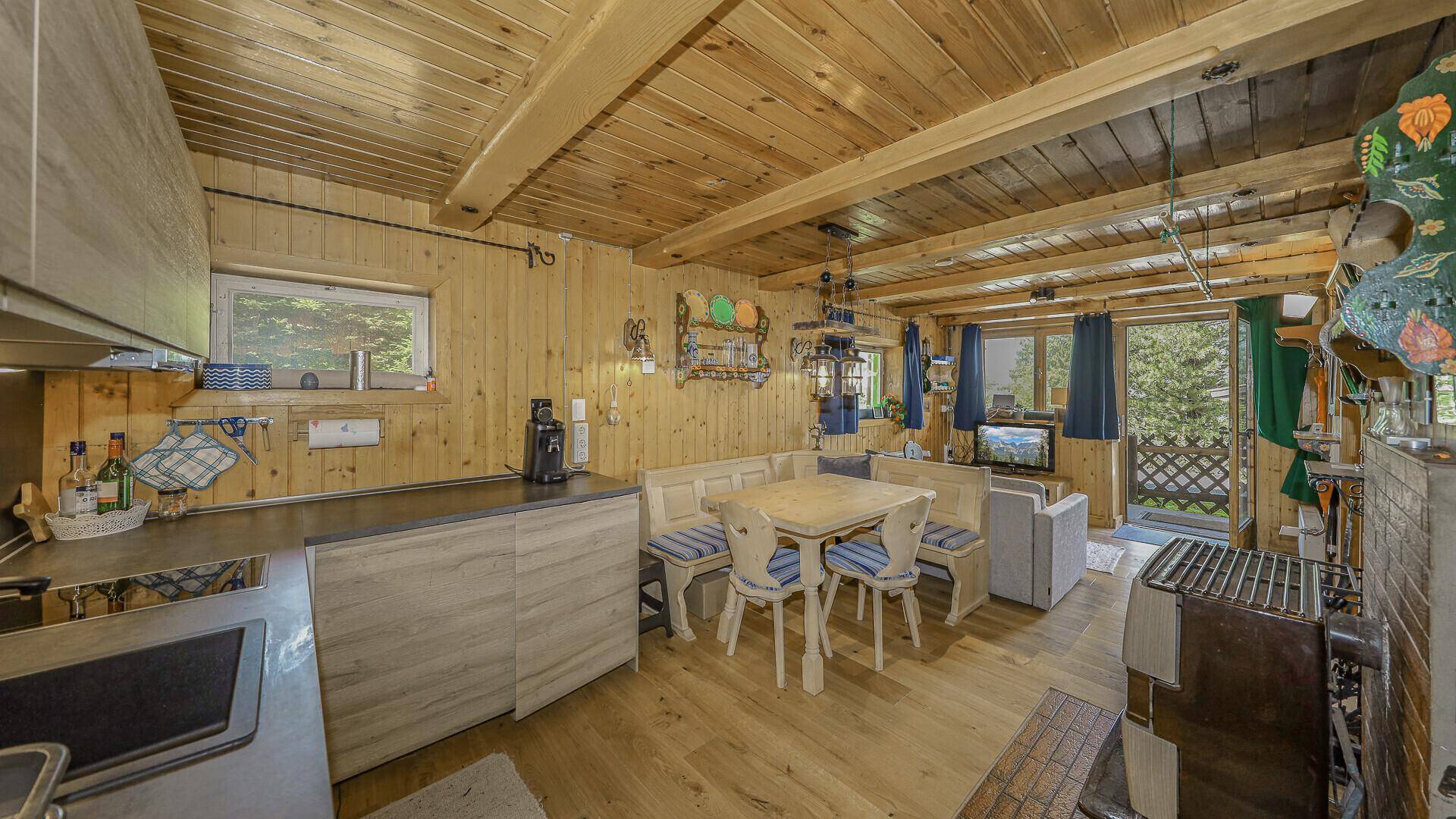 Gemütlicher offener Wohn-Essbereich mit Holztäfelung, kleiner Küche und traditionellem Ofen.