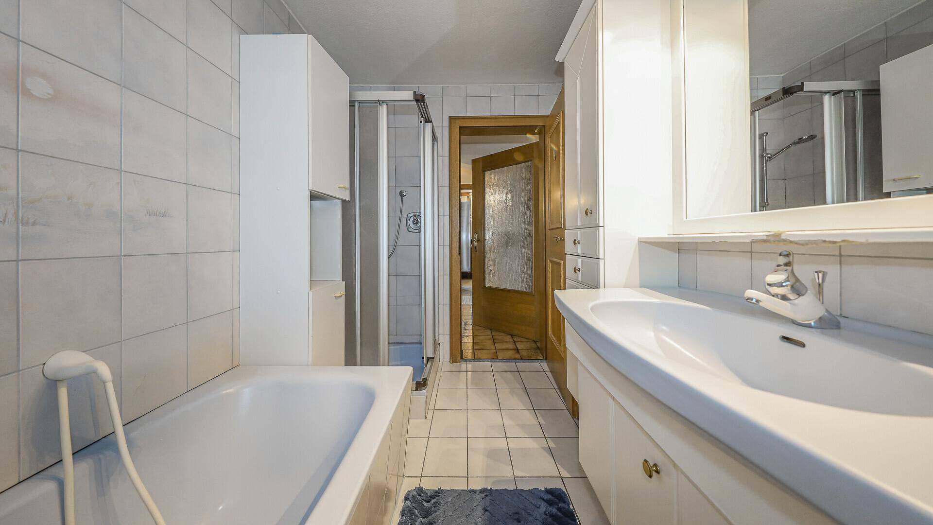 Helles Badezimmer mit Badewanne, Duschkabine und weißen Fliesen.