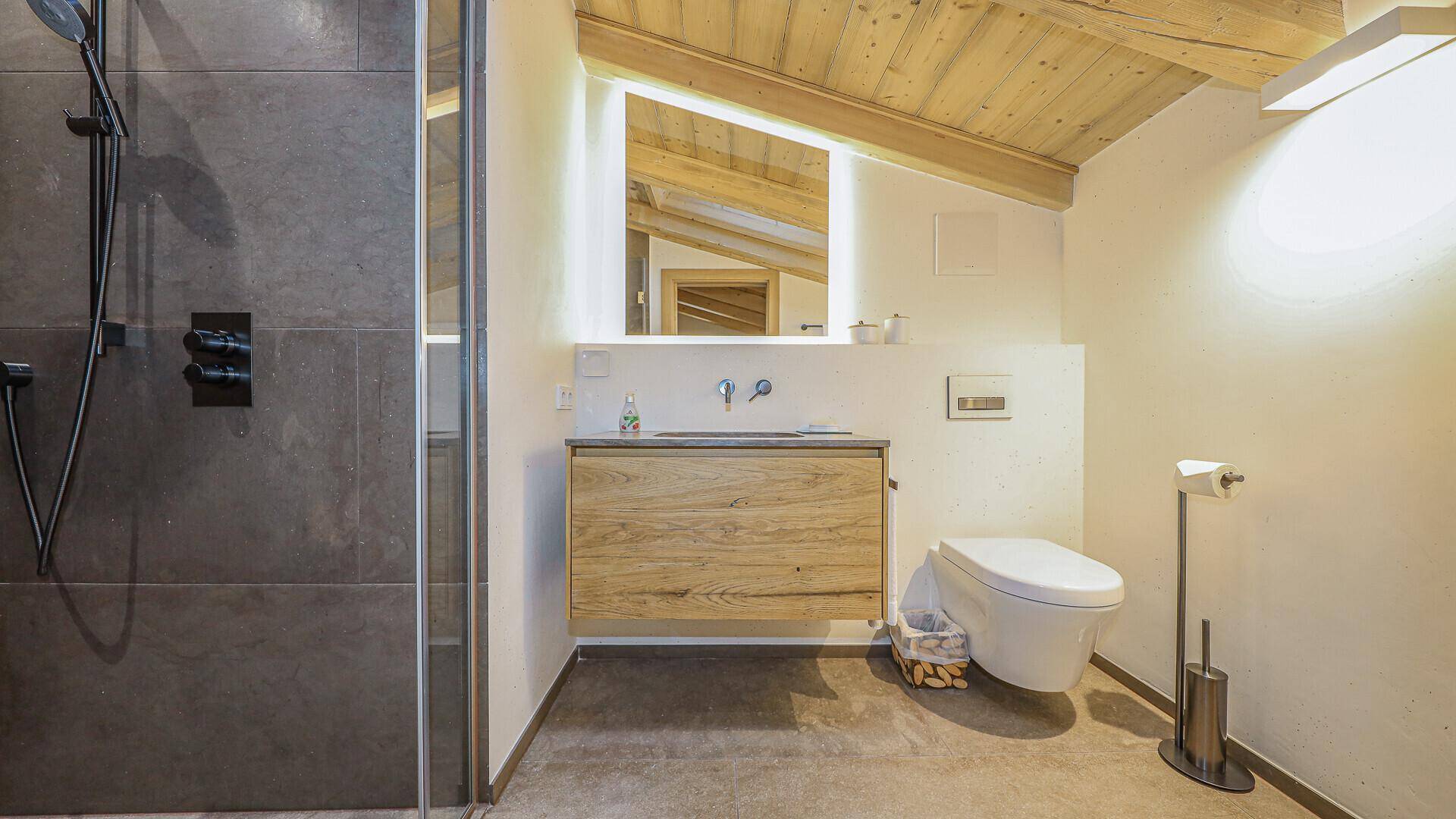 Modernes Badezimmer mit Dusche, wandhängendem WC und Holzwaschtisch im alpinen Stil.
