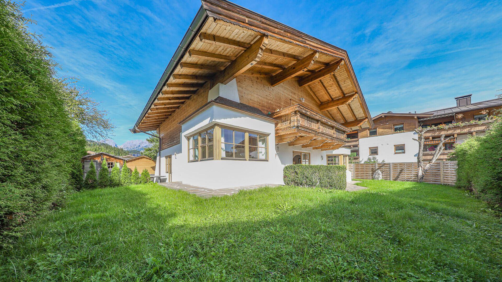 Seitenansicht des Chalets mit gepflegtem Rasen und Blick auf die Berge.