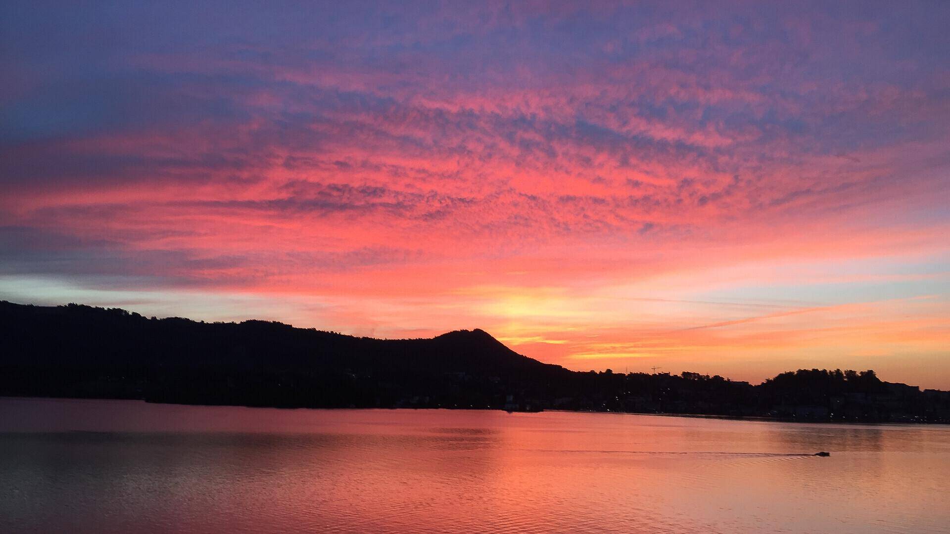 Farbenfroher Sonnenuntergang über einem See mit rosa und lila Tönen am Himmel und dunklen Bergen.