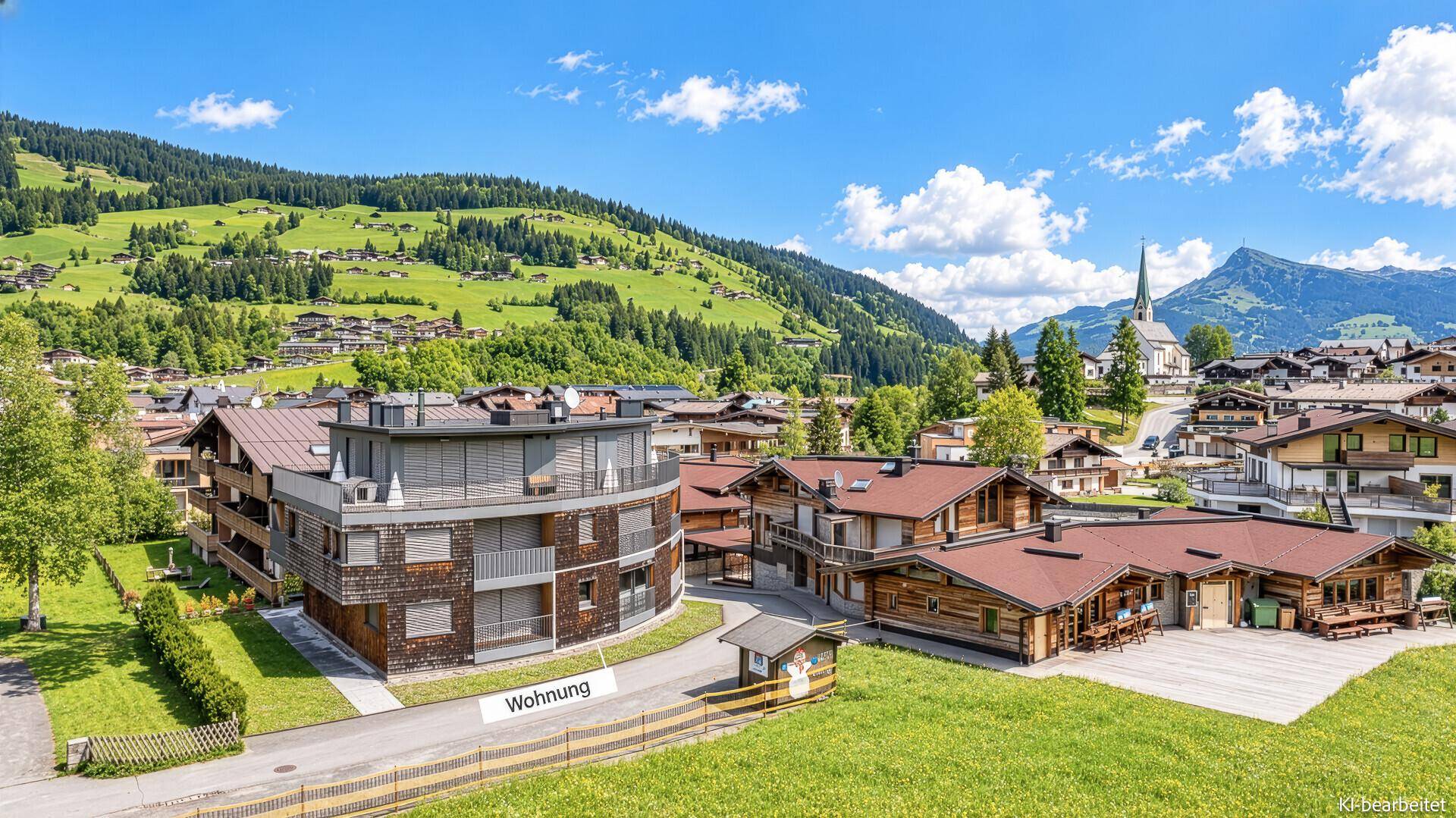 Luftaufnahme einer Wohnanlage in alpiner Umgebung mit grünen Hügeln.