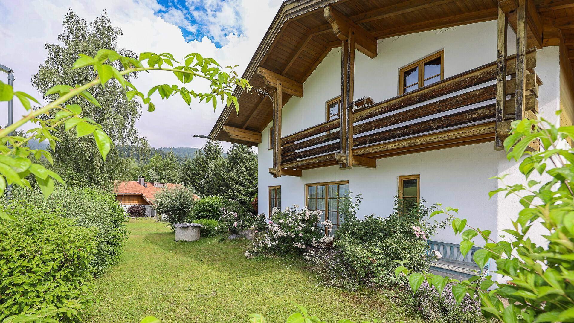Seitlicher Gartenbereich des Hauses mit blühenden Sträuchern und Blick auf die Fassade.