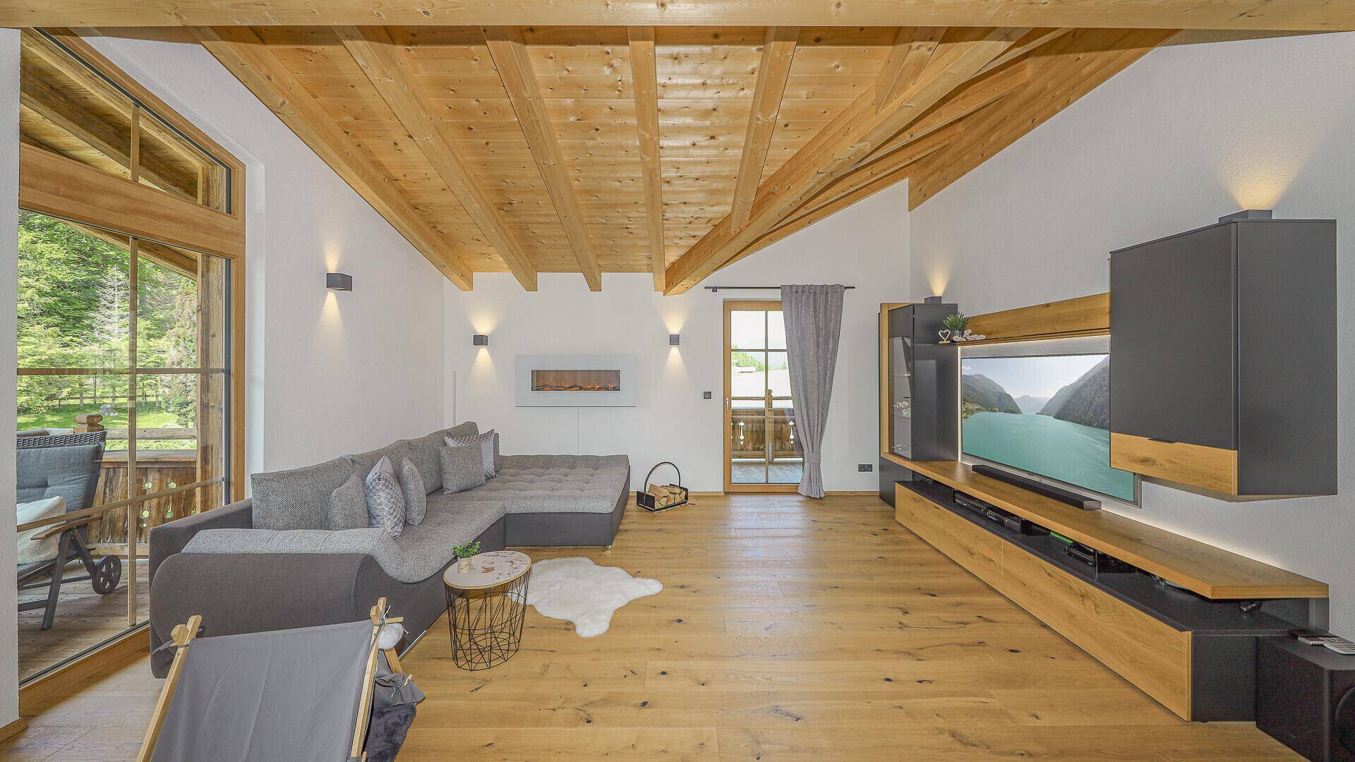 Lichtdurchfluteter Wohnbereich mit hoher Holzdecke, großem Sofa und Zugang zum Balkon.