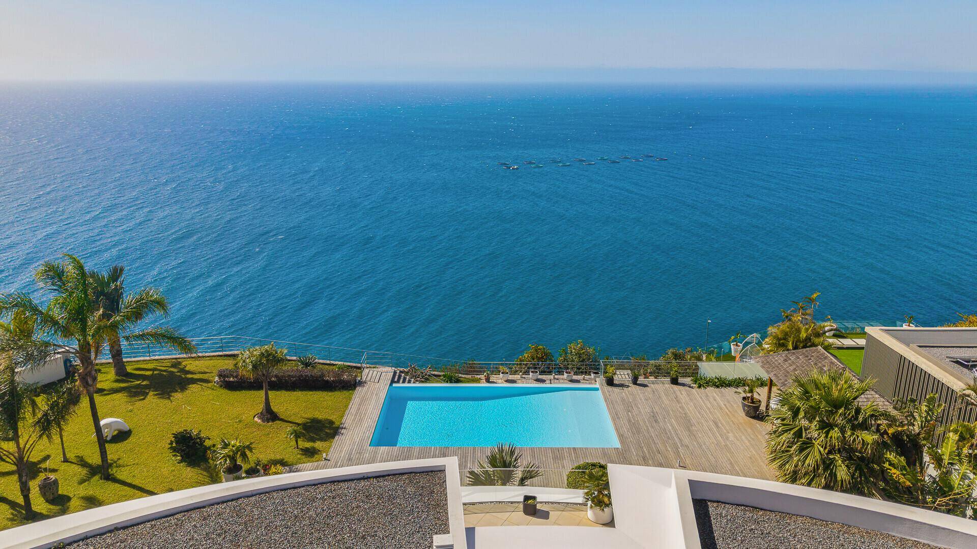 Exklusiver Außenbereich mit großem Pool, Holzdeck und Rasenfläche, direktem Blick auf das Meer.