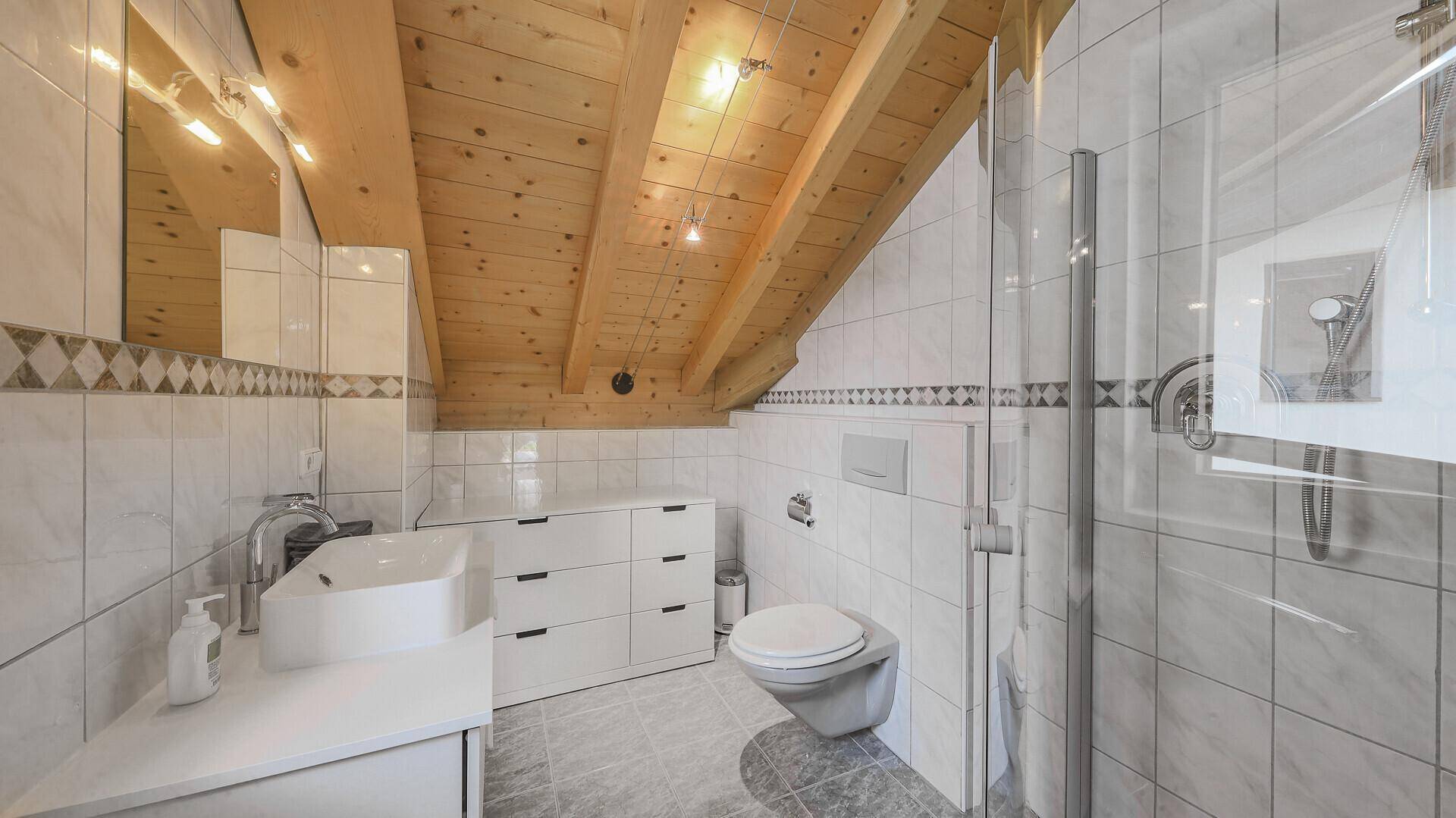 Modernes Dachbad mit Dusche, wandhängendem WC, Waschbecken und Holzbalkendecke.