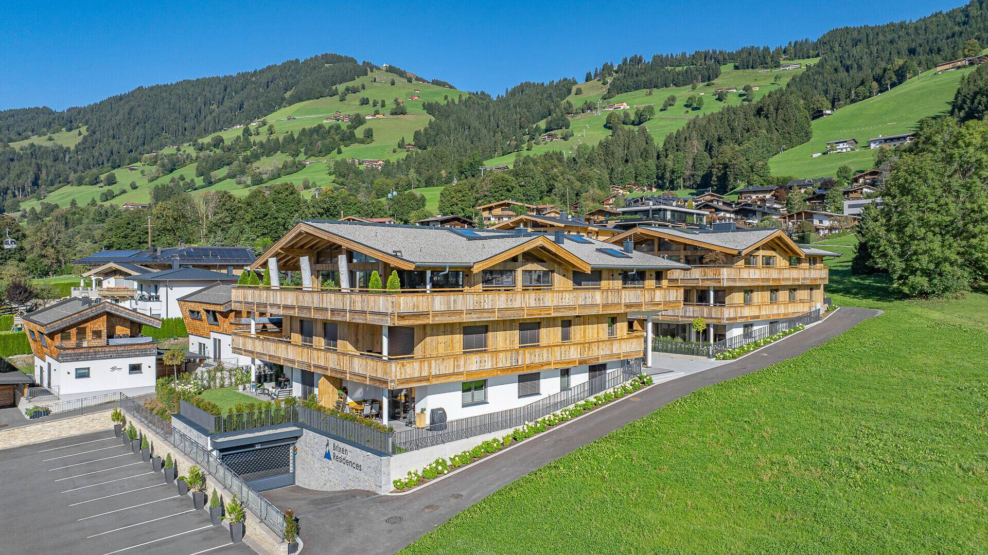 Gesamtansicht eines modernen Chalet-Komplexes mit Parkplätzen und grüner Umgebung.