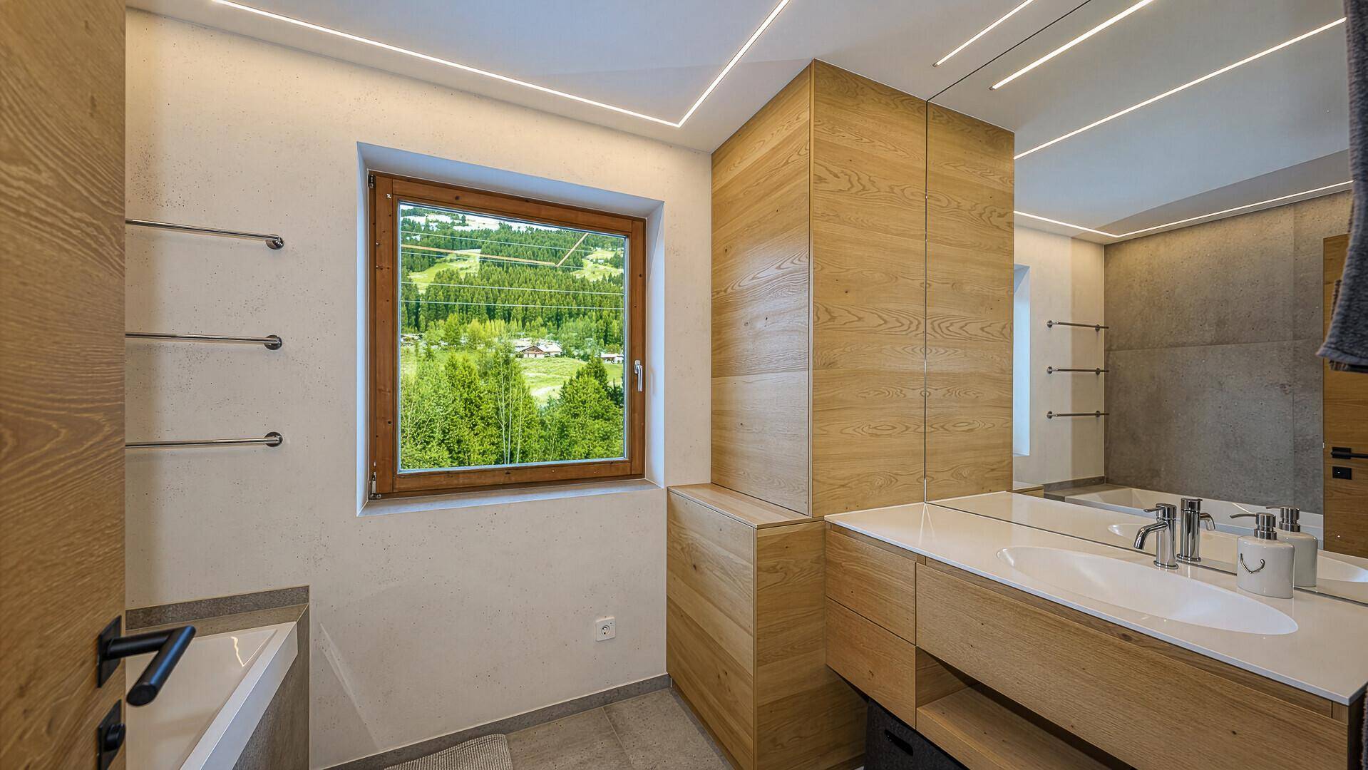 Modernes Badezimmer mit Holzwaschtisch, großem Spiegel und Fenster mit Blick ins Grüne.