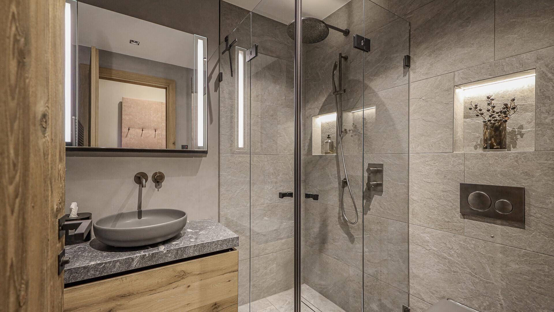 Modernes Badezimmer mit Einzelwaschbecken, begehbarer Dusche und grauen Fliesen.