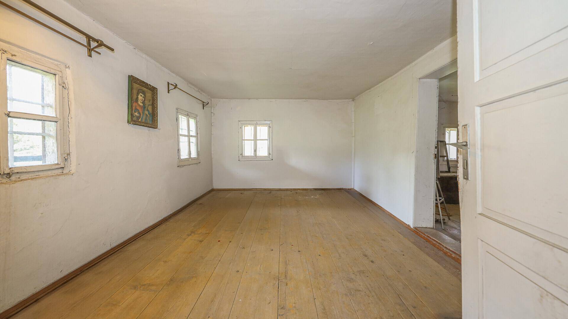 Leerer Raum mit Holzdielenboden und kleinen Fenstern, bereit zur Renovierung.