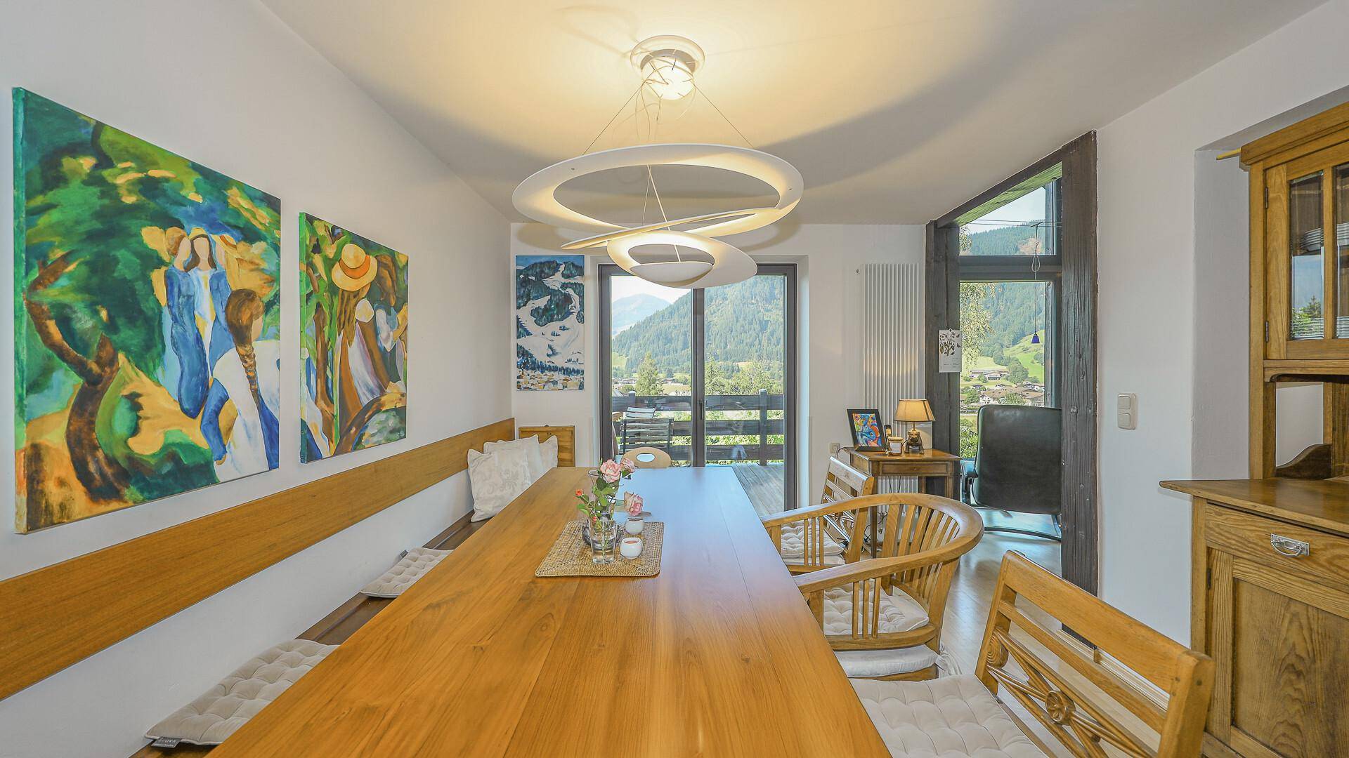 Heller Essbereich mit Holztisch, Sitzbank und Zugang zu einem Balkon mit Bergblick.