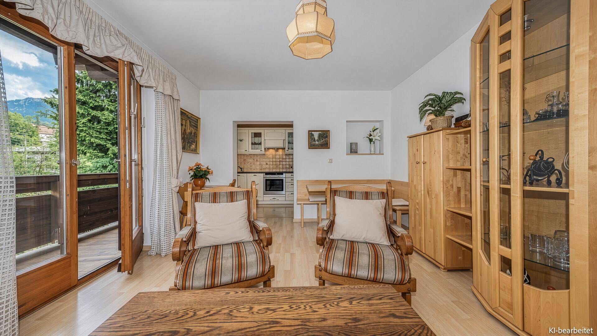 Helles Wohnzimmer mit traditionellen Holzmöbeln, Balkonzugang und Blick auf die Berge.
