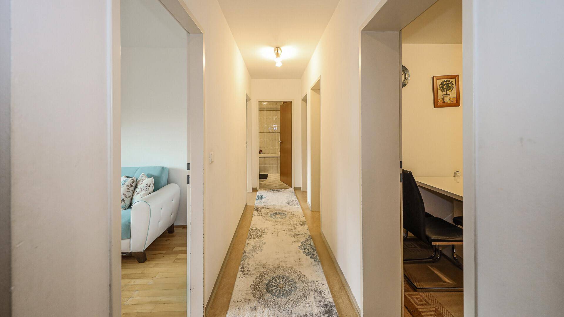 Heller Flur mit Teppichläufer, der zu verschiedenen Räumen führt, inklusive Bad und Schlafzimmer.