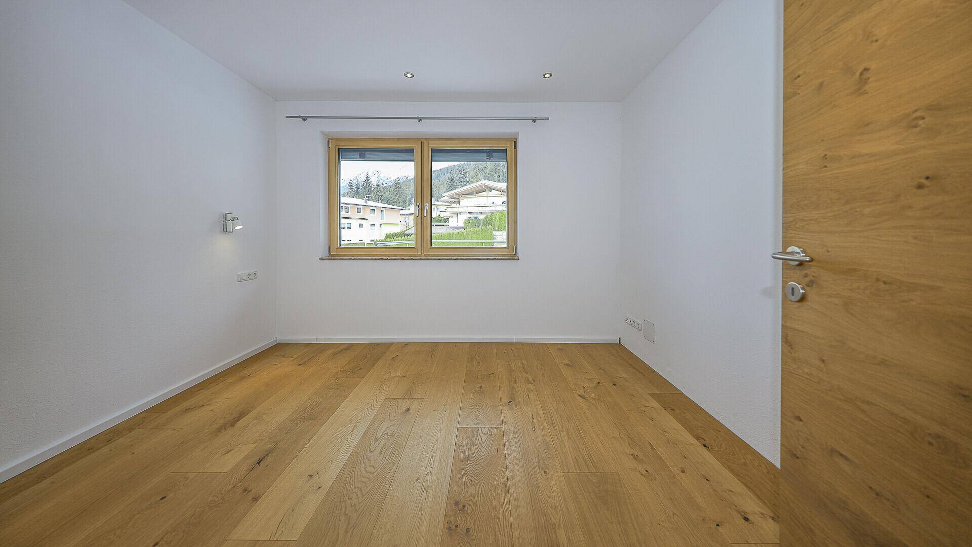 Helles Schlafzimmer mit Holzboden und Fenster mit Blick auf die Umgebung.