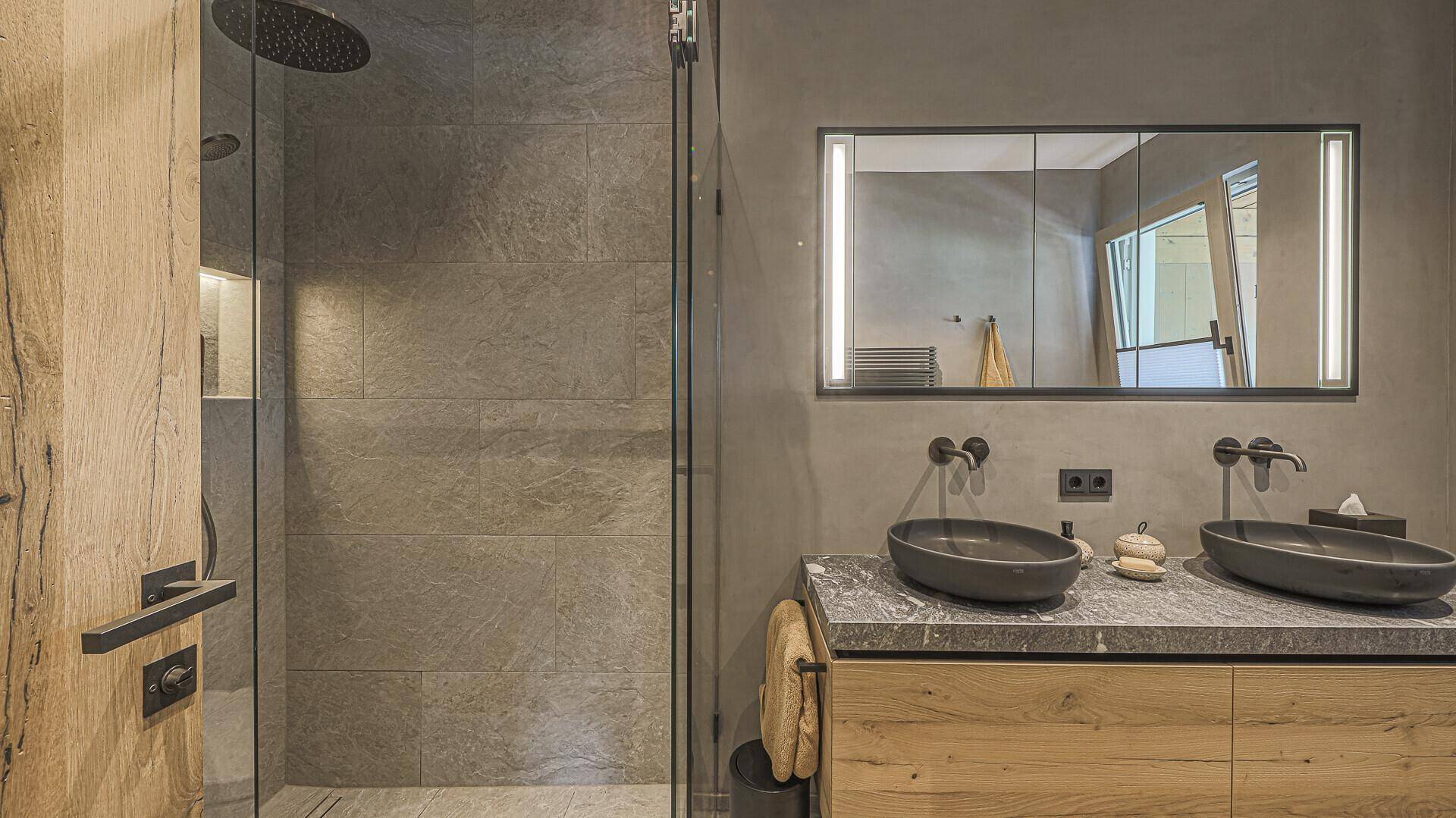 Modernes Badezimmer mit Doppelwaschbecken, begehbarer Dusche und beleuchtetem Spiegelschrank.