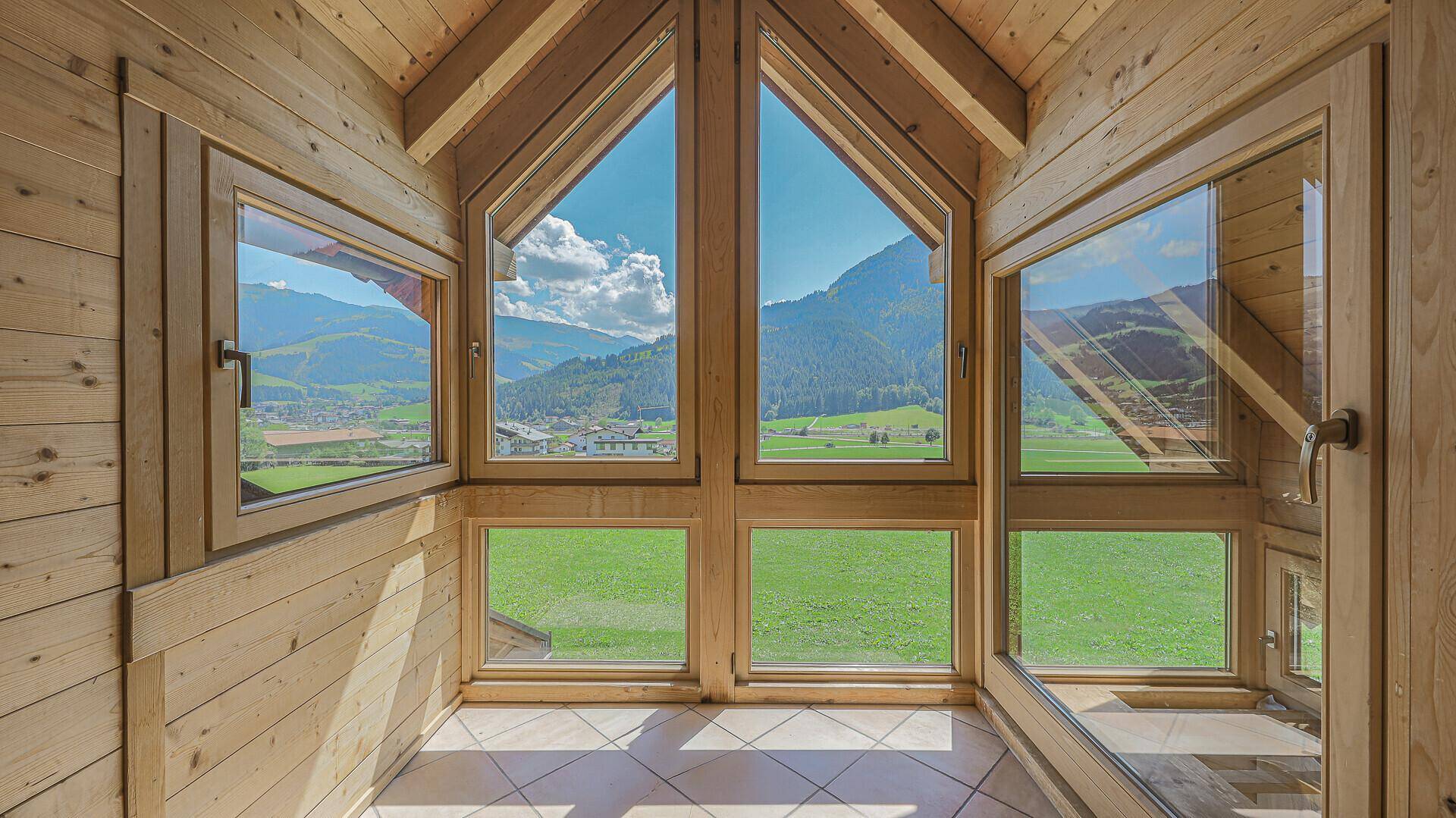 Heller Wintergarten mit Panoramafenstern, die einen beeindruckenden Blick auf die Berge und Felder bieten.