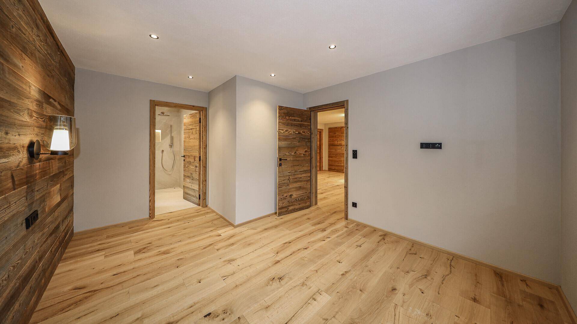 Geräumiges Schlafzimmer mit Holzwand und Holzboden, bietet Zugang zu einem modernen Badezimmer.