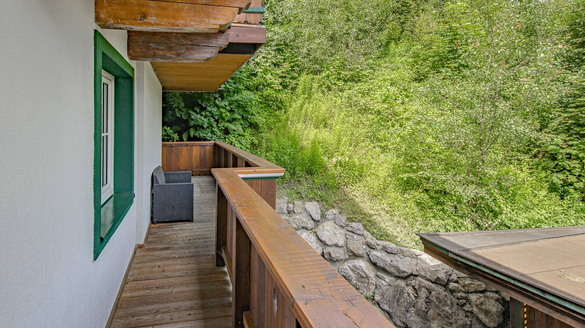 Langer Holzbalkon mit Blick ins Grüne und seitlicher Sitzgelegenheit.