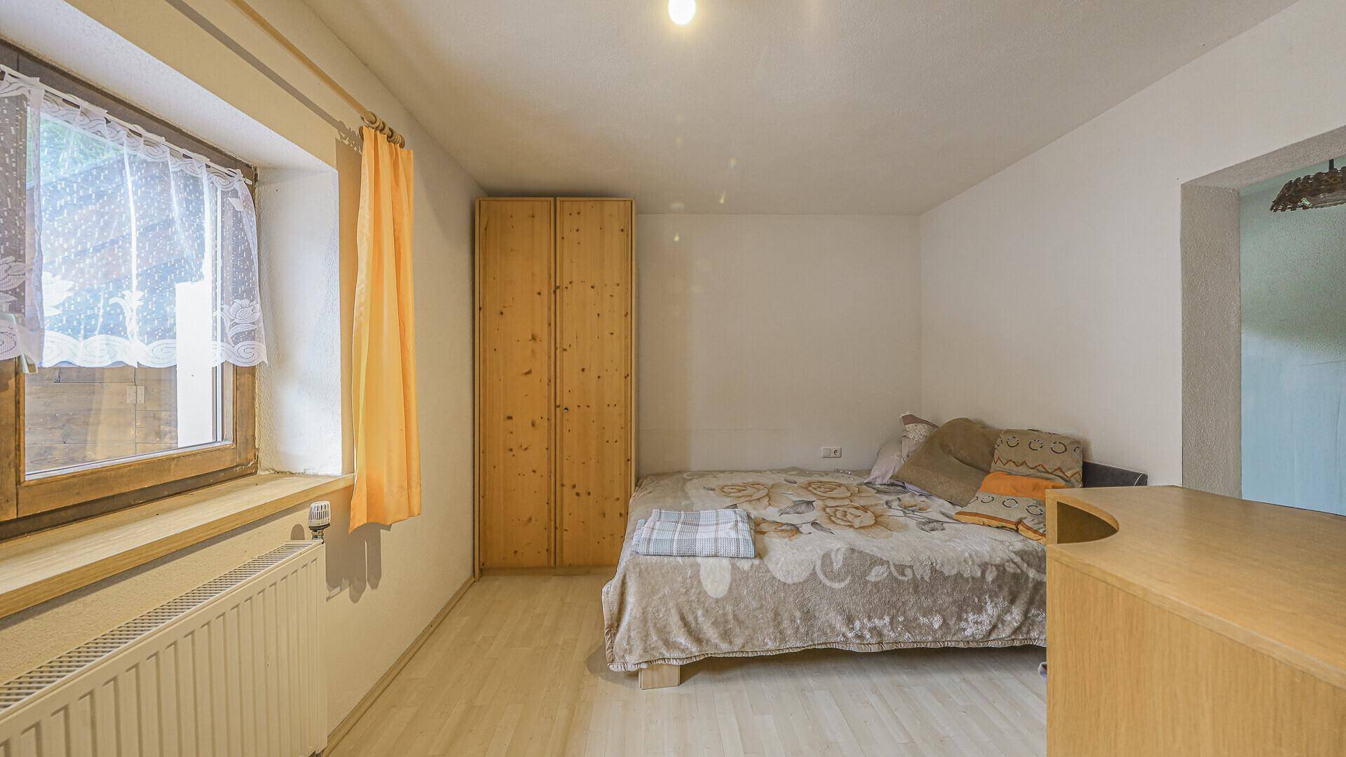 Einfaches Schlafzimmer mit Holzboden, Kleiderschrank und Fenster mit Vorhang.