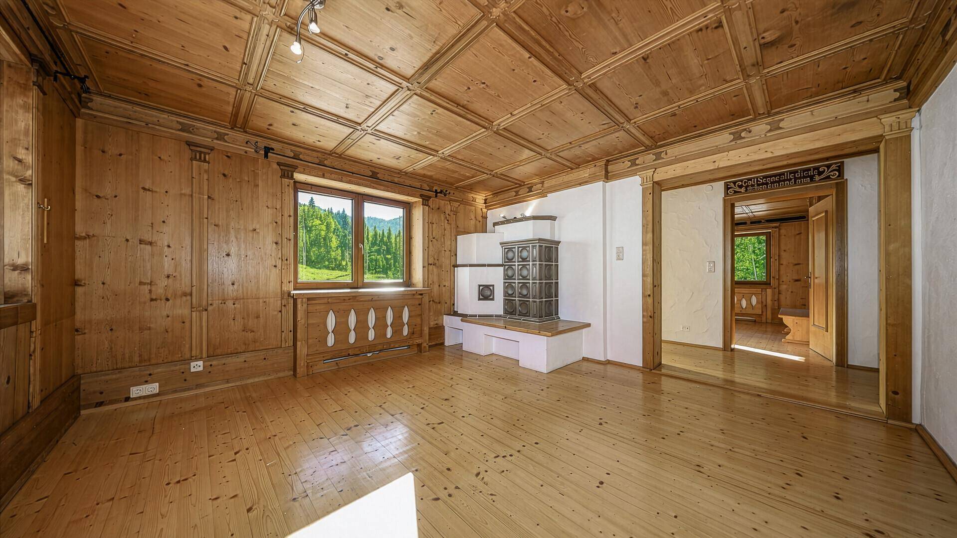 Geräumiges Wohnzimmer im alpenländischen Stil mit Holzboden, Holzvertäfelung und Kachelofen.