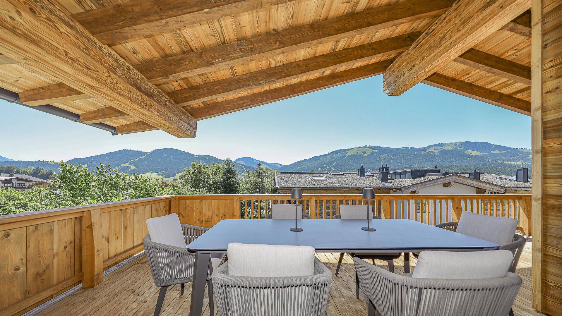 Großer überdachter Balkon mit Esstisch und Stühlen, ideal für Mahlzeiten im Freien mit Bergblick.