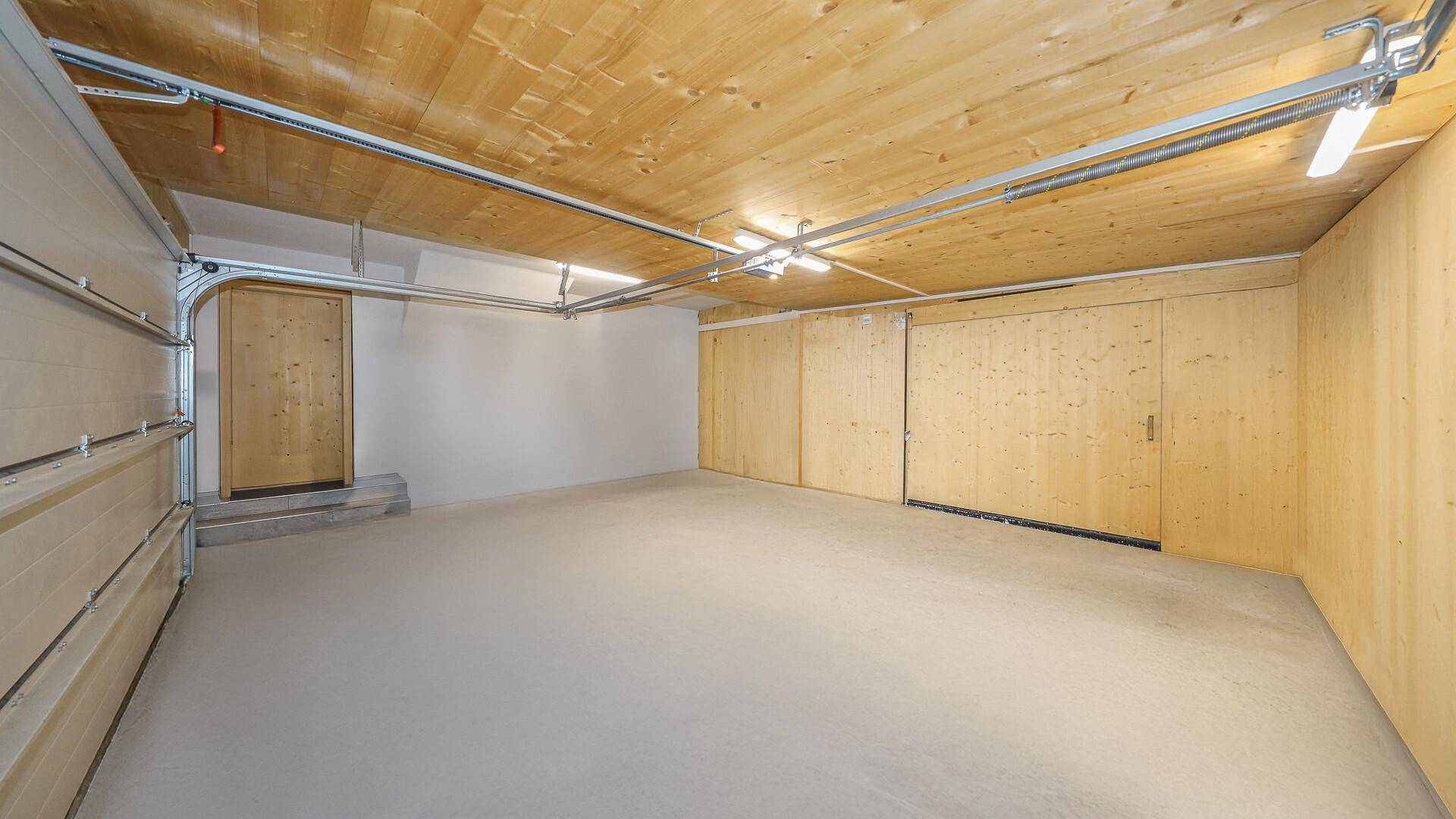 Geräumige Garage mit Betonboden und Holzwänden, bietet Platz für Fahrzeuge und Lagerung.